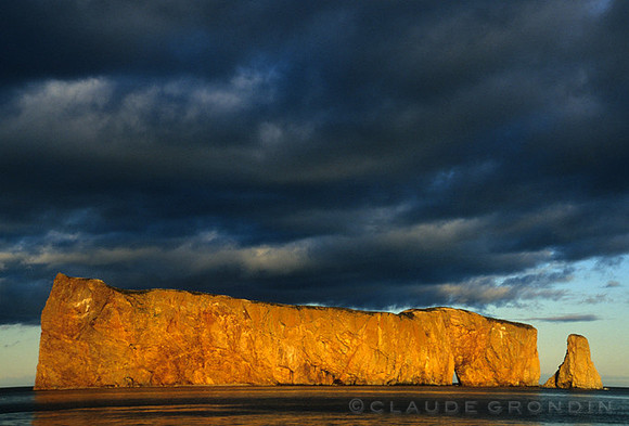 The Rocher Percé in Gaspésia is lit by the sunset light while a dark sky looks very threatening