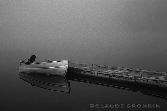 Image noir et blanc d'une chaloupe et d'un quai lors d'un matin très brumeux