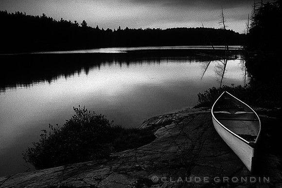 Image noir et blanc d'un canot blanc sur le rive d'un lac à l'aube